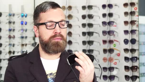 Älterer Mann wählt im Geschäft zwischen zwei Paar Sonnenbrillen - Filmmaterial, Video