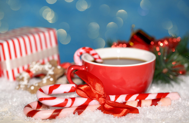 Hot tasty drink in red cup with Christmas candies on blue background - Photo, image