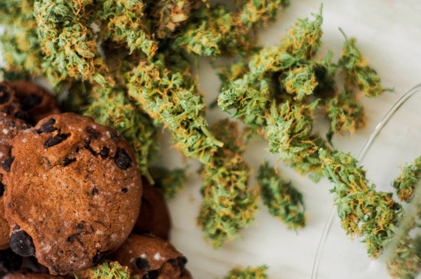 Koekjes met cannabis en toppen van marihuana bovenaanzicht op tafel. Concept van het koken met cannabis kruid. Behandeling van medische marihuana voor gebruik in levensmiddelen op een witte achtergrond - Foto, afbeelding