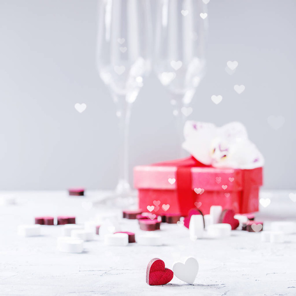 Love Valentine day or wedding greeting invitation card with two empty champagne glasses, red gift box, orchid flower, wooden hearts over white gray background. Space, selective focus. Square image - Fotoğraf, Görsel