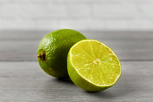 Whole lime and other one cut in half, on a gray wooden table. - Valokuva, kuva