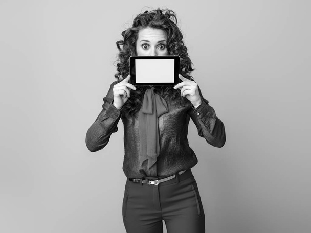 surprised stylish woman with long wavy brunette hair hiding behind tablet PC blank screen - Foto, Bild