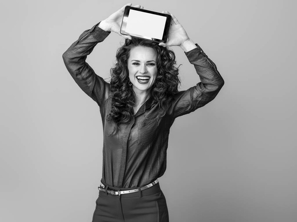 lächelnde junge Frau mit langen welligen brünetten Haaren, die Tablet-PC-Bildschirm leer zeigt  - Foto, Bild