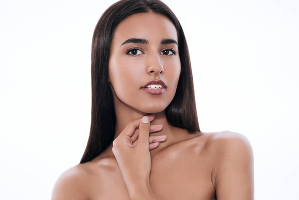 Beautiful close-up portrait of attractive young brunette woman looking at the camera, with hand on neck, with long hair, on white background. Cosmetics. Make-up. Spa. Stomatology - Φωτογραφία, εικόνα