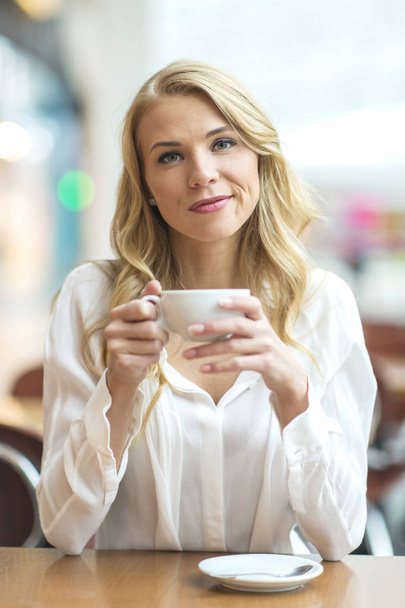 Young blonde sitting in a cafe, drinking coffee and looking into - Foto, Imagem