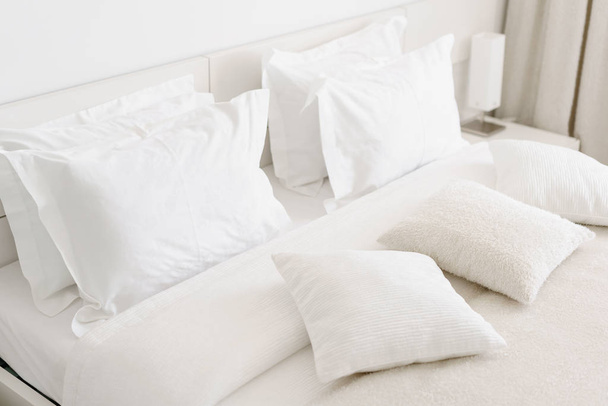 Cómodas almohadas suaves en la cama. Sábanas blancas de primer plano y almohada en el fondo de la habitación de la pared de luz. concepto de cama fresca
 - Foto, Imagen