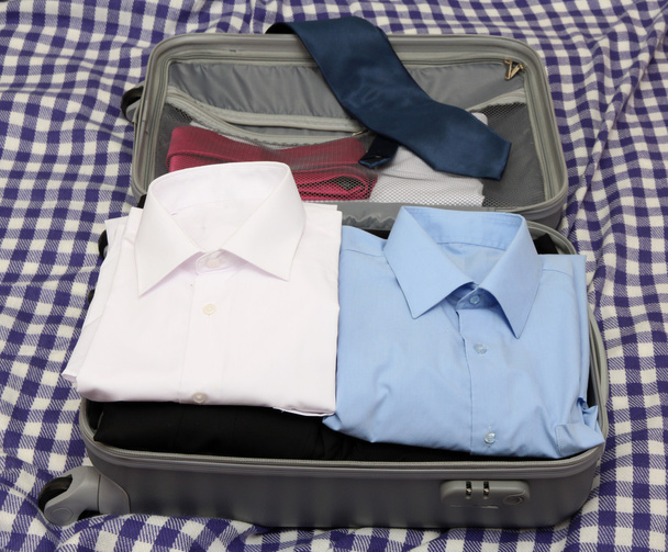 Open grey suitcase with clothing on plaid - 写真・画像