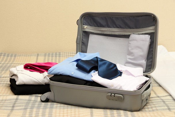 Open grey suitcase with clothing on bed - Foto, immagini