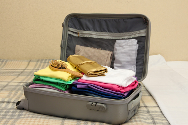 Open grey suitcase with clothing on bed - Foto, Bild