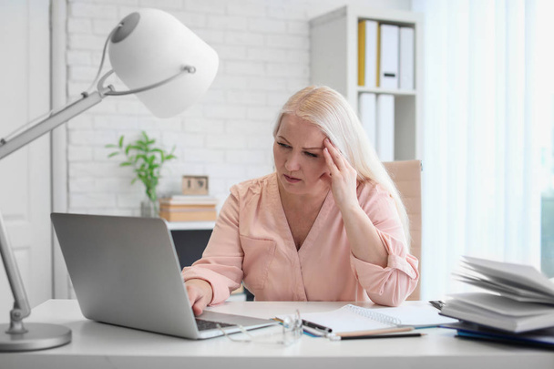 Érett nő szenved fejfájás hivatalban asztalnál ülve - Fotó, kép
