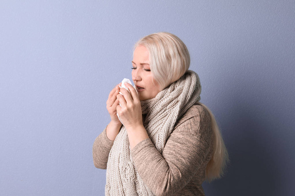 Mature woman with tissue suffering from cold on color background - Foto, Imagem