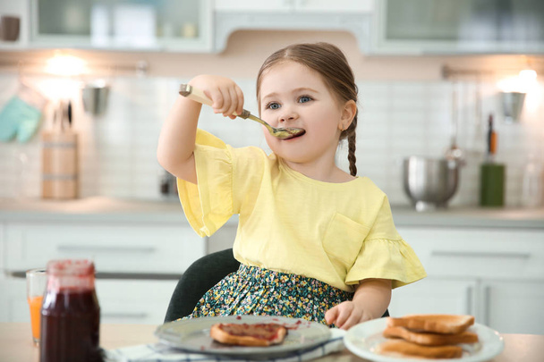 Little girl eating jam at table in kitchen - 写真・画像