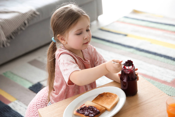 Little girl with jam and toasts in living room - Fotó, kép