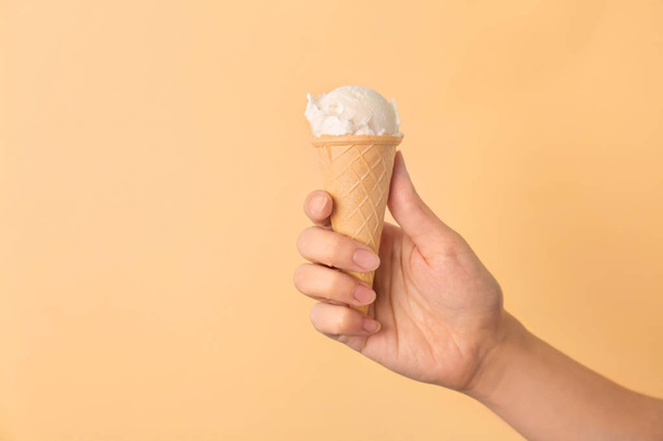 Woman holding waffle cone with tasty vanilla ice cream on color background - Foto, immagini