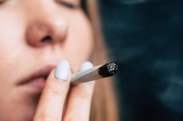 Konzepte des medizinischen Marihuanakonsums und der Legalisierung von Cannabis. Rauch auf schwarzem Hintergrund. eine Frau raucht Cannabiskraut, einen Joint und ein Feuerzeug in seinen Händen. - Foto, Bild