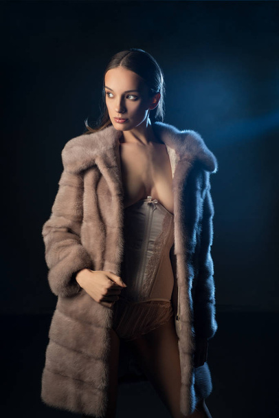 Pretty brunette topless in fur coat in the dark - Фото, изображение