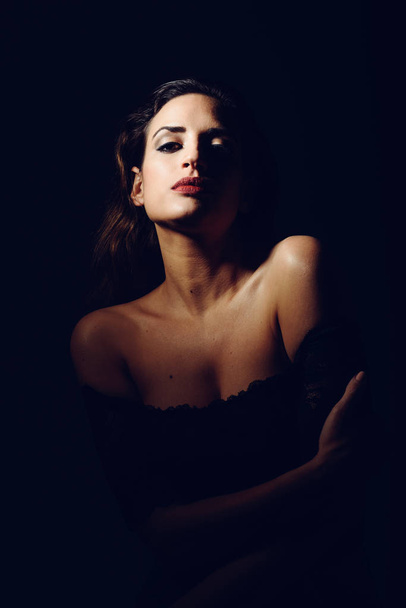 Young brunette woman in black lingerie in chiaroscuro lighting - Fotografie, Obrázek
