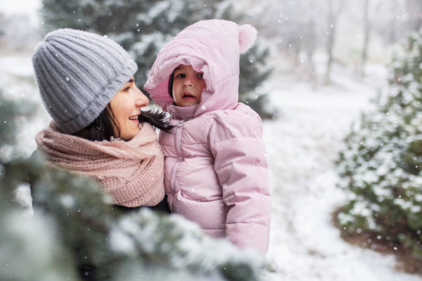 Beautiful portrait of happy smile mother with her toddler girl, outdoors in park or forest on snowing day.Winter mood. Family portrait. Motherhood and childhood - Foto, Bild