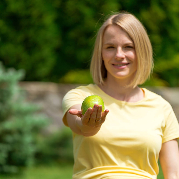Pregnant woman sitting on grass and holding out apple in hand - Photo, Image
