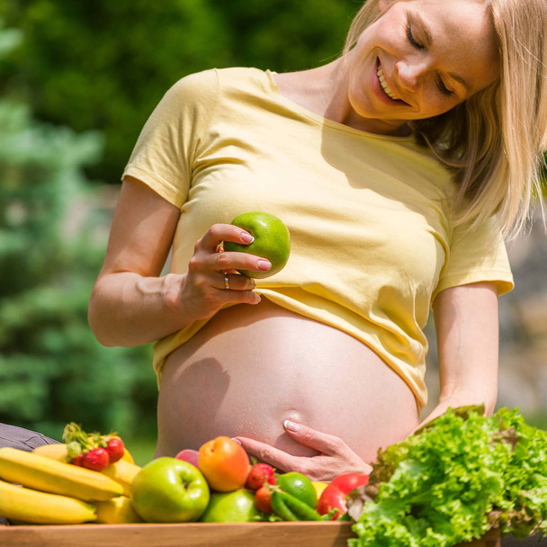 Pregnant woman sitting on grass and holding an apple in hand - Foto, imagen