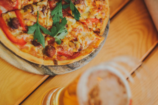 Pizza savoureuse et verre de bière sont sur la table en bois
 - Photo, image