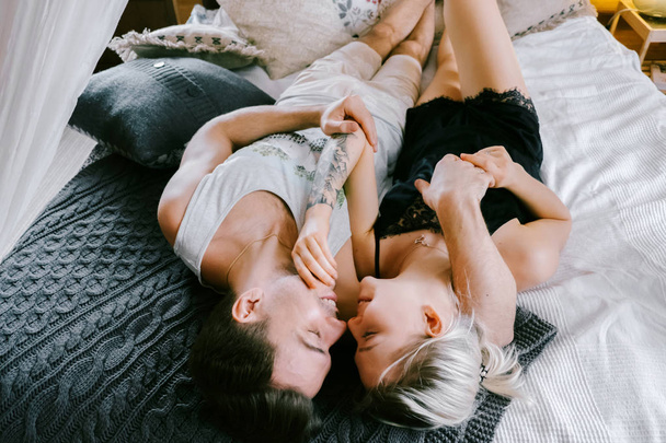 Lovely couple together at home. Pretty woman and attractive man wearing home clothes lying on a bed, kissing and hugging. - Fotó, kép