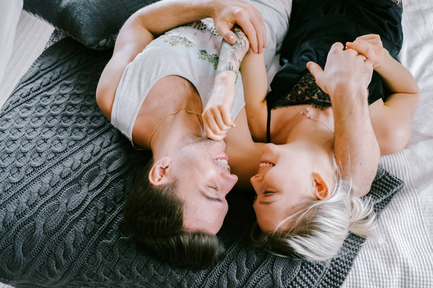 Lovely couple together at home. Pretty woman and attractive man wearing home clothes lying on a bed, kissing and hugging. - Fotografie, Obrázek