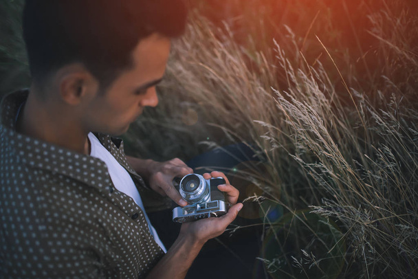 View from above of an adorable close-up portrait of a young man with vintage camera on field, grass, nature, background. Travel. Picture for background. Autumn. Summer - Foto, afbeelding