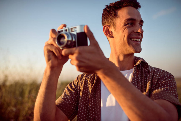 Beautiful portrait of handsome smile young man with vintage camera,on a meadow background. Travel mood. Photography. Relaxation on a field and sunset. Explore nature. - Foto, Imagem