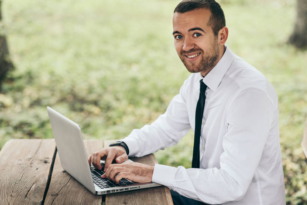 Mosolygó jóképű férfi ül a fa tábla segítségével a laptop, hogy elégedett, őszinte mosoly, míg a szörfözés az interneten, fehér ing. Emberek, karrier, érzelmek, technológia koncepció.  - Fotó, kép