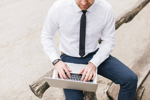 Кроппы сняты умным красивым мужчиной в белой рубашке, сидящим за деревянным столом, используя ноутбук и беспроводной интернет во время серфинга в Интернете. Человек, карьера, эмоции, технологическая концепция
.  - Фото, изображение