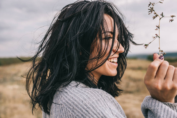 Side view portrait of happy brunette young woman wearing gray sweater being playful and carefree with beautiful smile  and windy hair posing on landscape. Lifestyle concept. Cover idea mood. - Foto, afbeelding