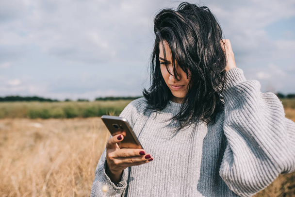 Smart and pretty Caucasian woman texting on mobile phone, using wireless connection for social life, posing outside with windy hair and feeling free. Copy space. People, travel and lifestyle concept. - Fotoğraf, Görsel