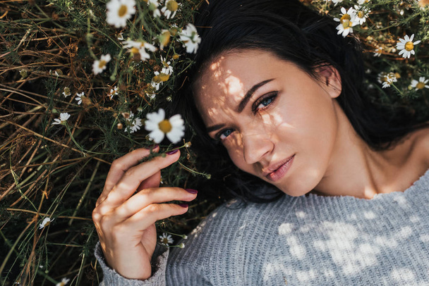 Close-up portrait of a beautiful woman on meadow looking to the camera and enjoying nature spring evening outdoors. Caucasian woman relaxation in the park with daisy outside with copy space, cover - Foto, afbeelding