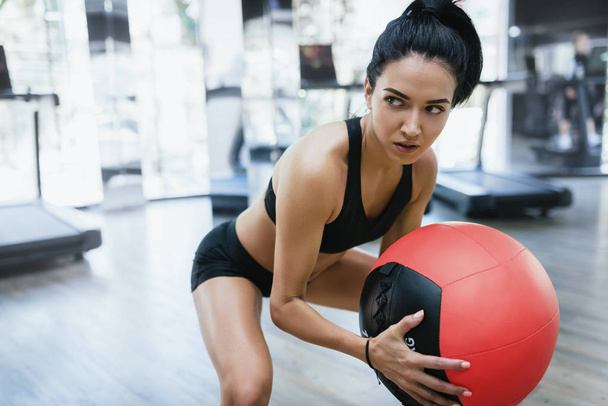 Portrait of muscular athletic woman doing squats workout in gym. Strong female squatting  on fitness mat with weight medicine ball in health club. Sport, people and lifestyle concept. - Фото, зображення