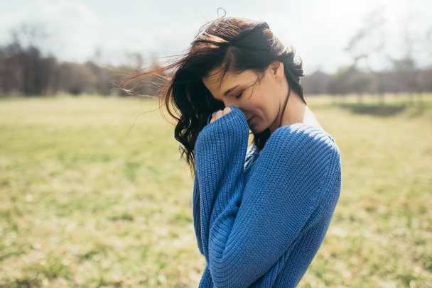 Horizontal portrait of attractive brunette caucasian young woman with windy hair, dreaming outside, on spring or on summer, in park. Female with closed eyes in blue pullover. Lifestyle cover concept. - Zdjęcie, obraz
