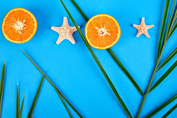 Έννοια καλοκαίρι. Πορτοκαλί φρούτα, αστερίες και palm φύλλα σε φόντο μπλε χαρτί. Επίπεδη θέσει. Χώρο αντίγραφο - Φωτογραφία, εικόνα