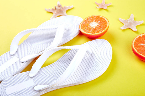 Conceito de verão. Chinelos brancos, fruta laranja, estrela do mar em fundo de papel amarelo. Deitado. Espaço de cópia
 - Foto, Imagem