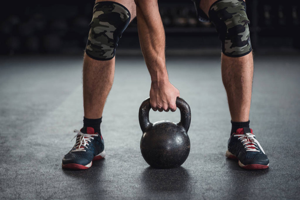 Man is holding grabbing a kettle bell in a cross fit gym - Photo, Image