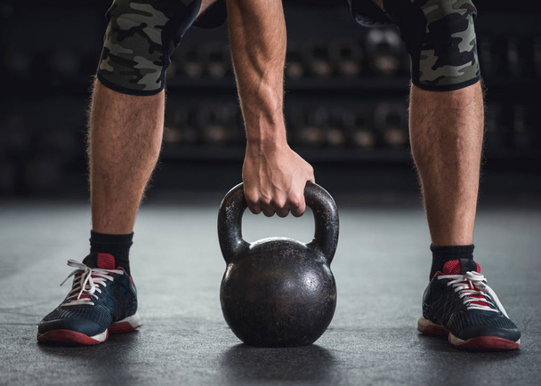 Man is holding grabbing a kettle bell in a cross fit gym - Photo, Image
