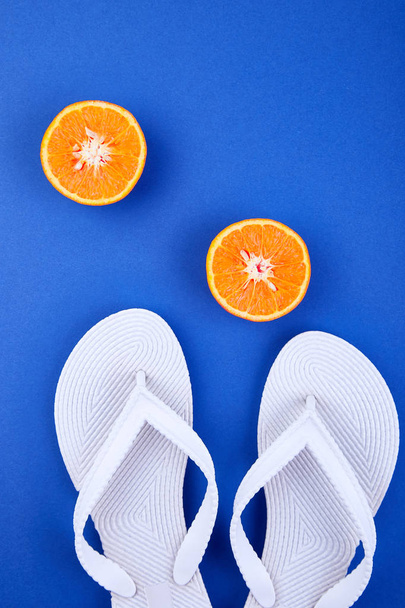 Kesäkonsepti Valkoiset sandaalit, appelsiinit, simpukat sinisellä paperilla. Litteä pano. Kopioi tila
 - Valokuva, kuva