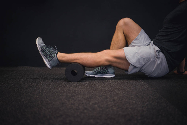 Hombre usando un rodillo de espuma en el suelo en el gimnasio
 - Foto, Imagen