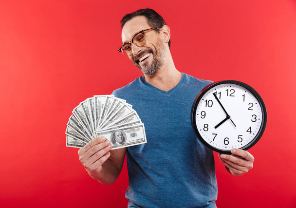 Adult cheerful positive man holding money and clock. - 写真・画像