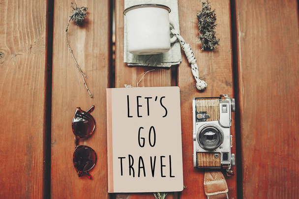 let's go travel text on notebook, wanderlust concept. map with sunglasses, photo camera, mug, notebook on wooden background, top view. stylish traveler hipster set flat lay - Photo, Image