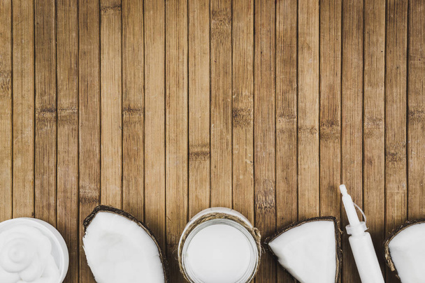 Coconut pieces and cosmetics on a wooden table. Coconut milk cream and butter. Copy space for text - Photo, Image