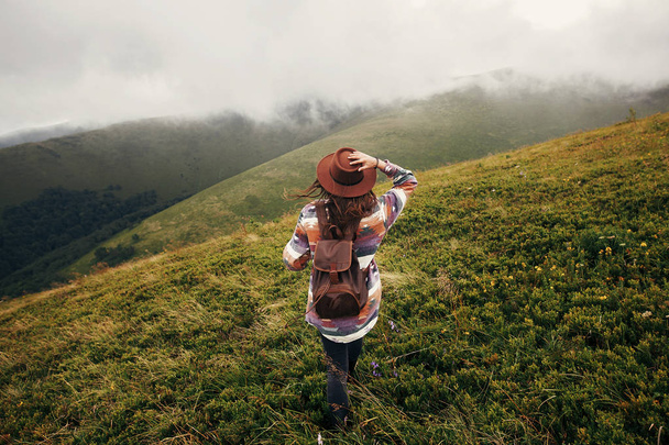 流行の旅行者のバックパックを雲の晴れた山を見て帽子の女の子。夏休み。旅と放浪癖の概念。テキストのためのスペース。背面図。素晴らしい大気瞬間 - 写真・画像