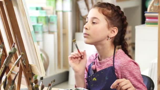 Söpö pieni tyttö näyttää peukalot ylös maalatessaan kuvaa taidekurssilla
 - Materiaali, video