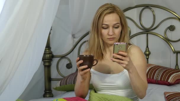 femme gaie assise au lit dansant et chantant, buvant du café et bavardant avec des amis sur un téléphone. 4K
 - Séquence, vidéo