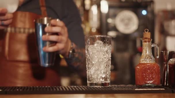 Bar-Regal mit hohem Glas mit Eiswürfeln drinnen, Barmann bewegt sich im Hintergrund - Filmmaterial, Video