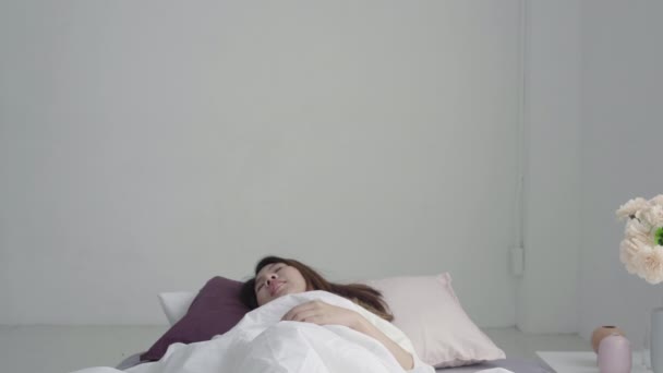 Happy beautiful young Asian woman waking up in morning, sitting on bed, stretching in cozy bedroom, looking through window. Funny asian woman after wake up. Asia woman is stretching and smiling. - Imágenes, Vídeo